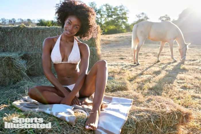 Tanaye White sits on a blanket in a field in a white bikini.